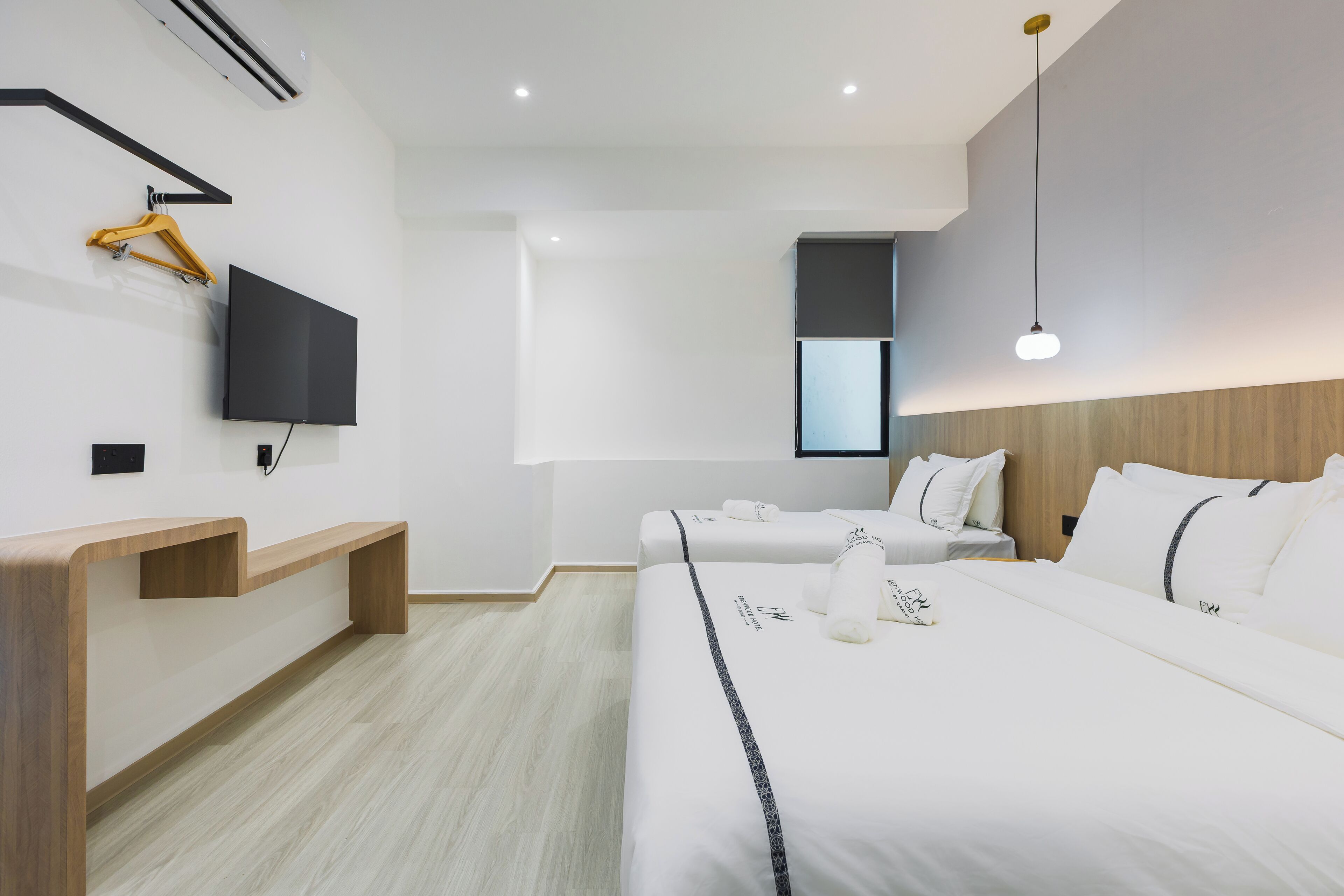 A modern hotel room with a large bed, a TV mounted on the wall, a wooden bench, and a window providing a view of the outside.