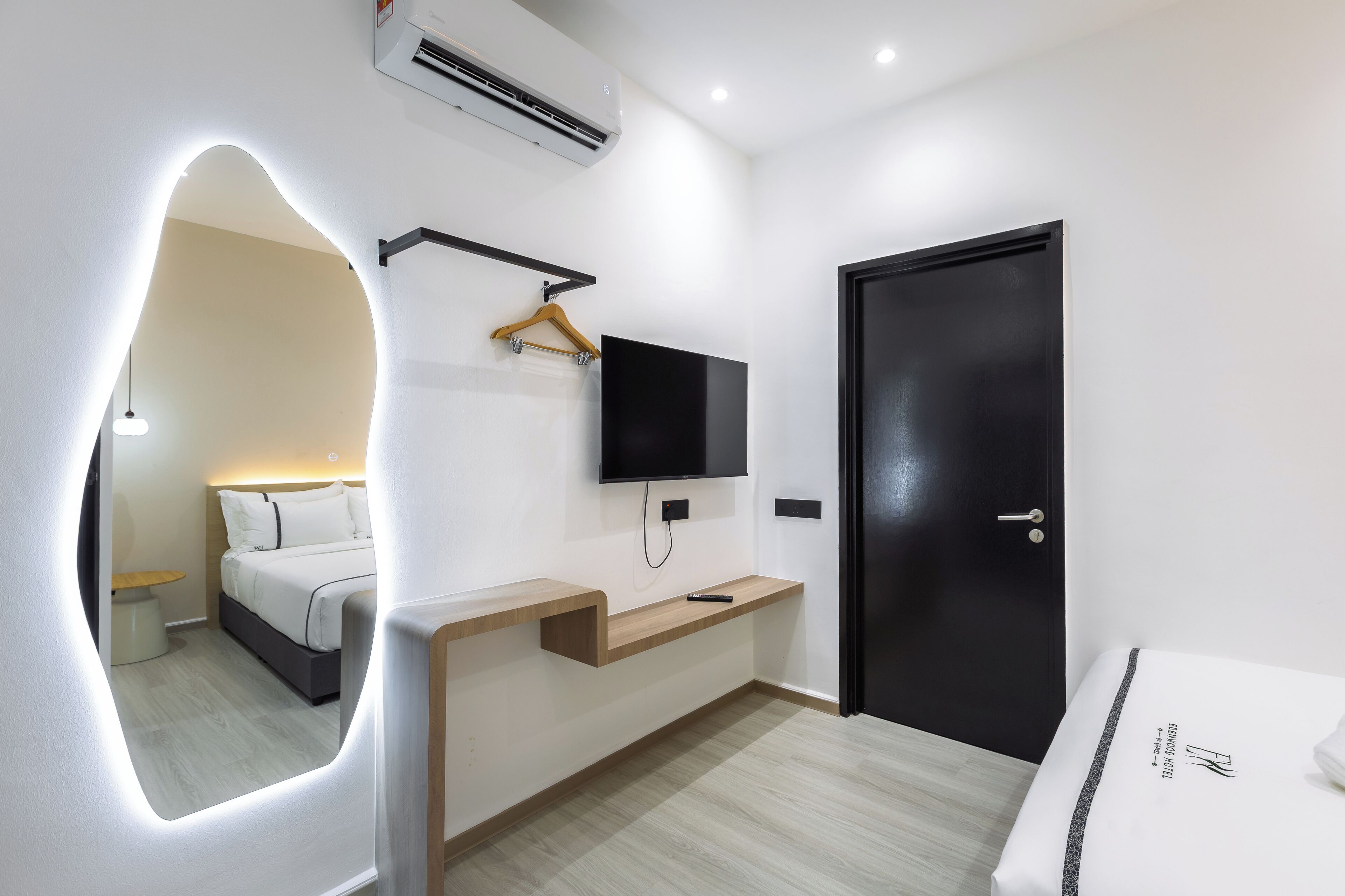 Une chambre d’hôtel moderne avec un lit, un téléviseur fixé au mur, une table de chevet en bois et une porte noire.