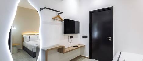 Une chambre d’hôtel moderne avec un lit, un téléviseur fixé au mur, une table de chevet en bois et une porte noire.