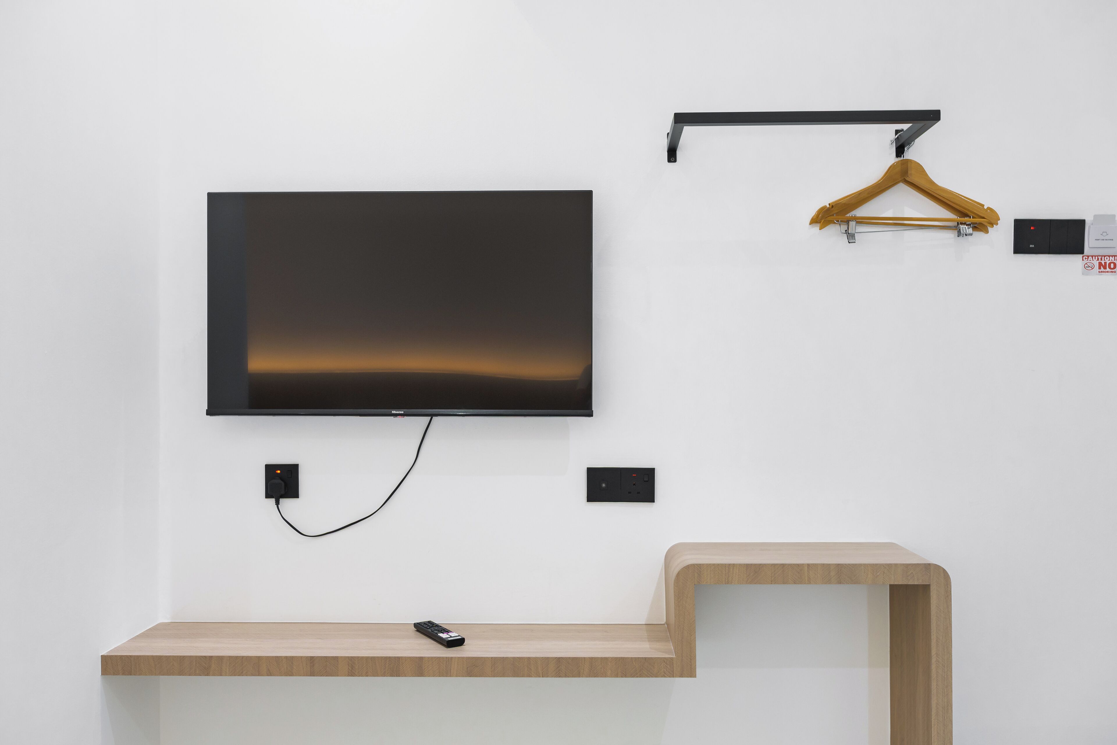 A modern room with a mounted flat-screen TV, a wooden console table, a wall-mounted hanger, and electrical outlets.