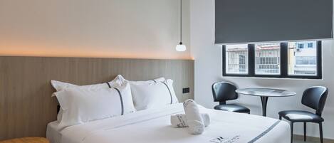 A hotel room with a neatly made bed, a round table, two chairs, and a window with a view of buildings.