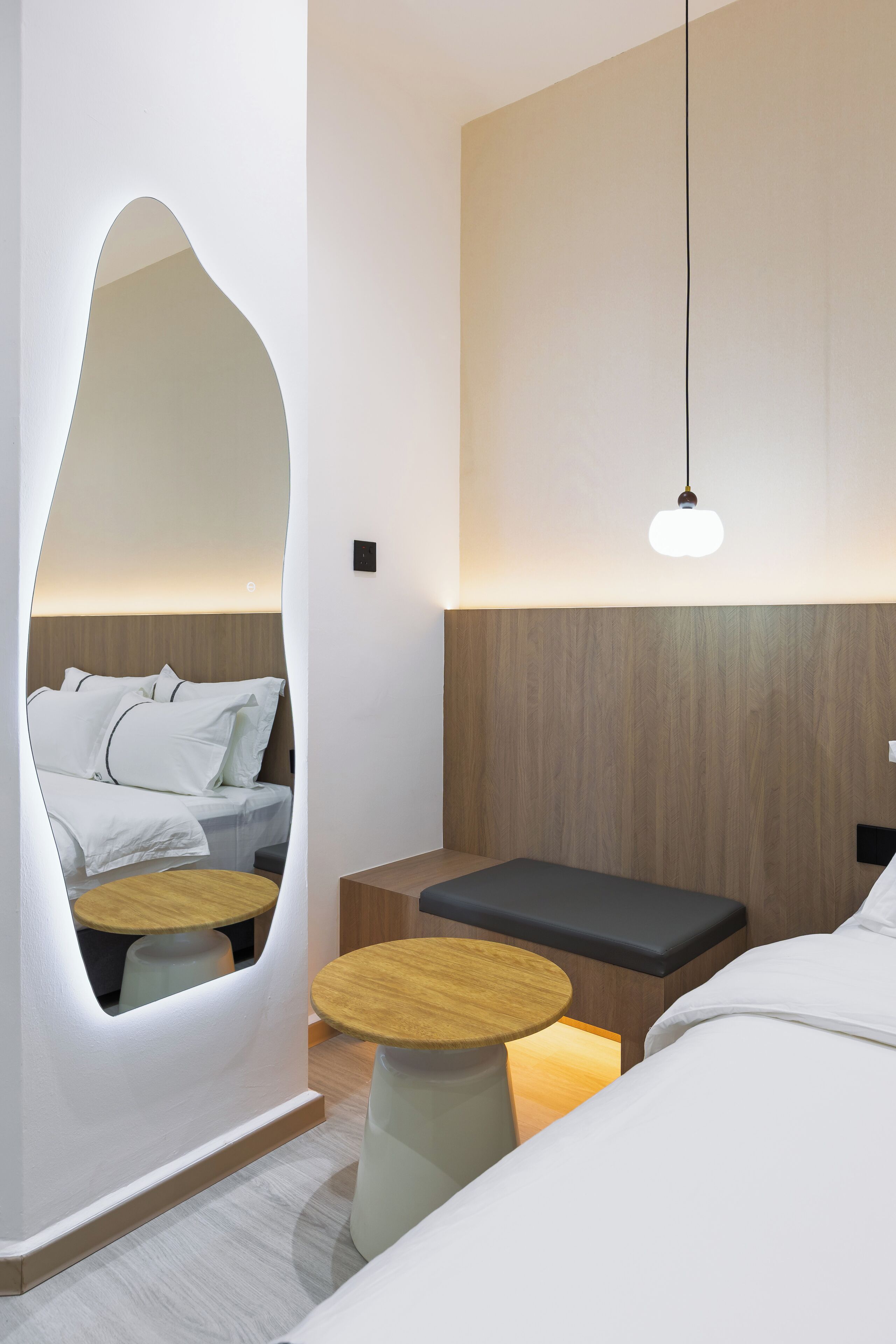 Una habitación de hotel moderna con una cama, una mesita de madera, un banco y un elemento decorativo único en la pared.