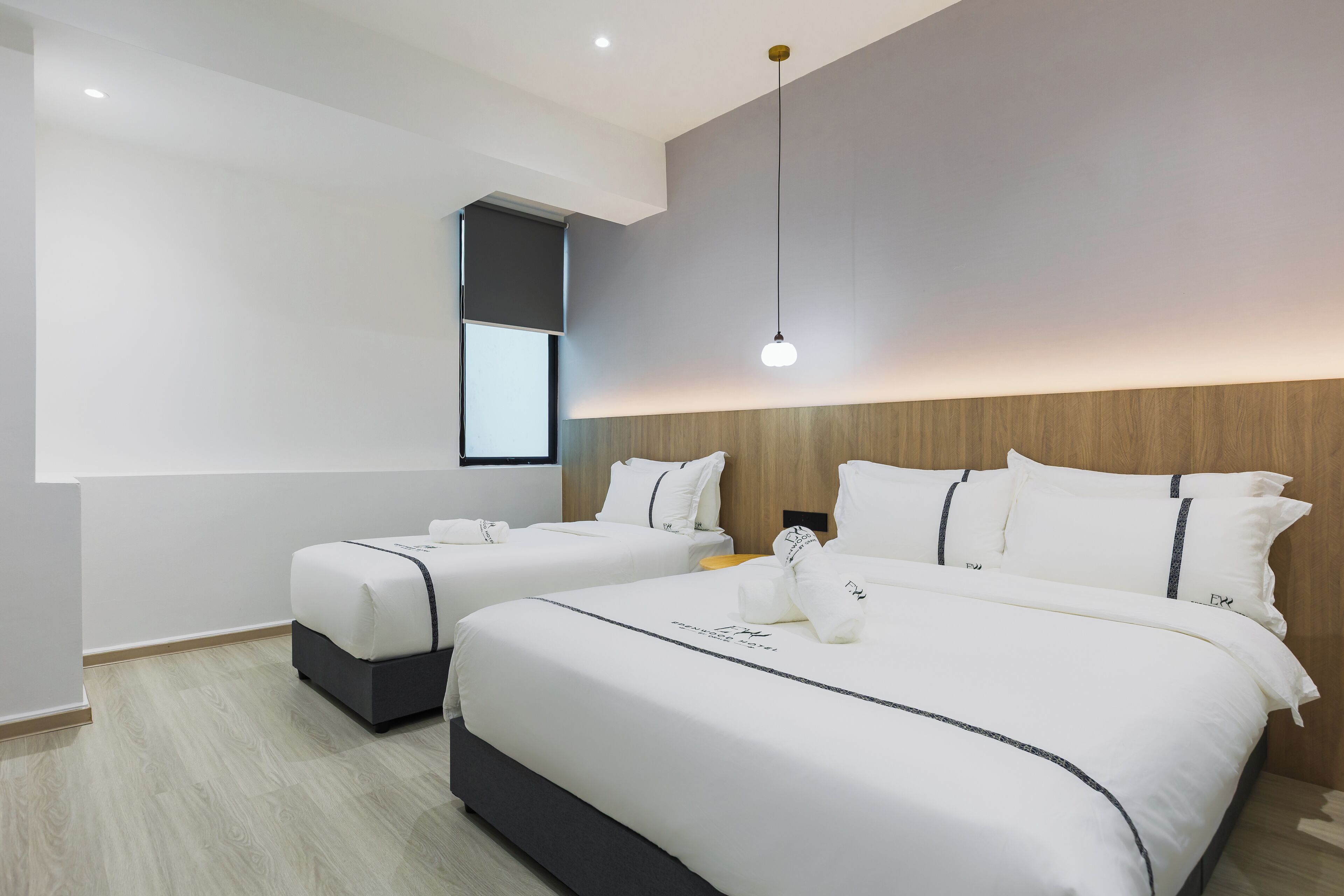 A modern hotel room with two beds, a wooden headboard, and a pendant light.