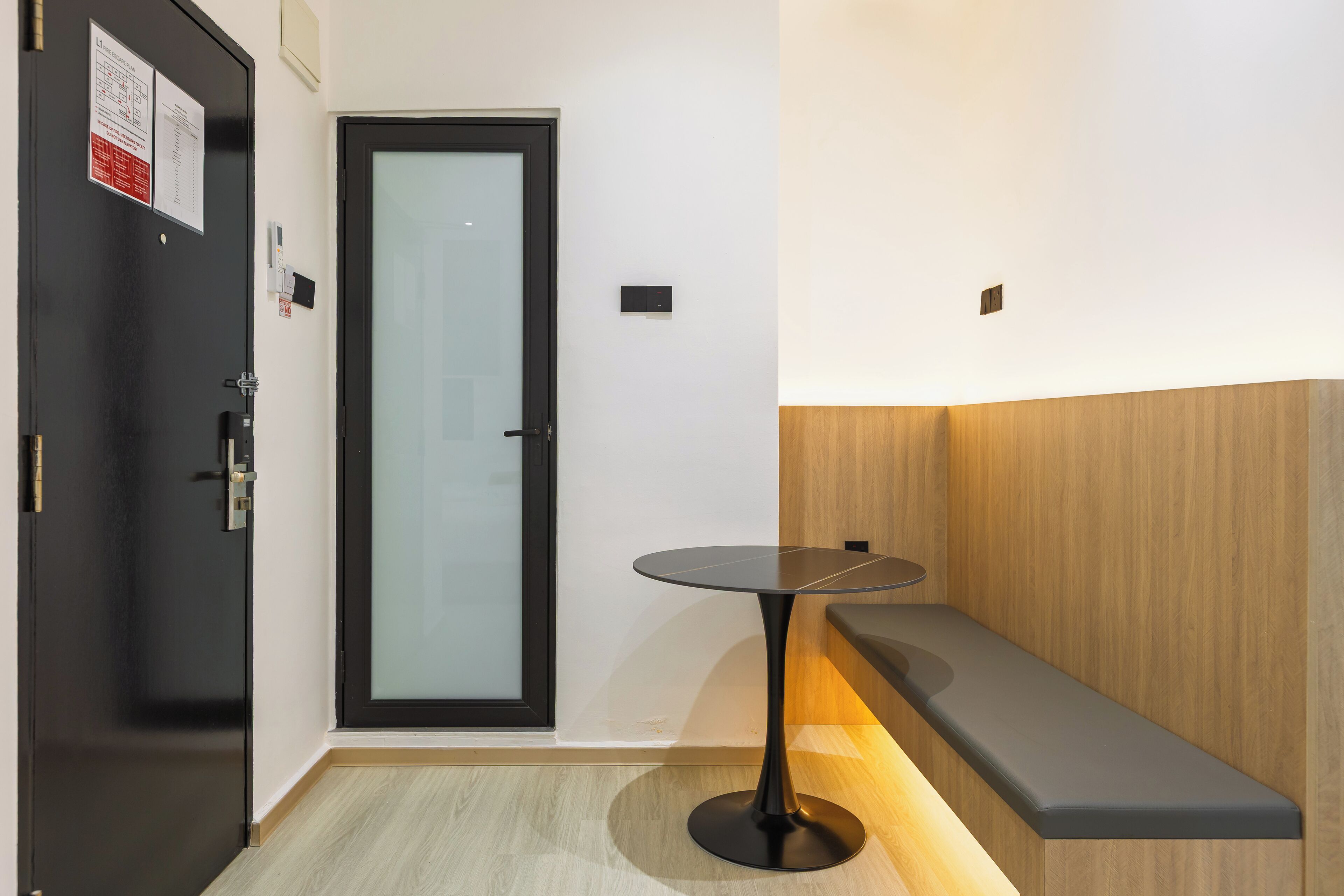 Un moderno vestíbulo de hotel con una puerta negra, una puerta de cristal, una mesa redonda y un banco.