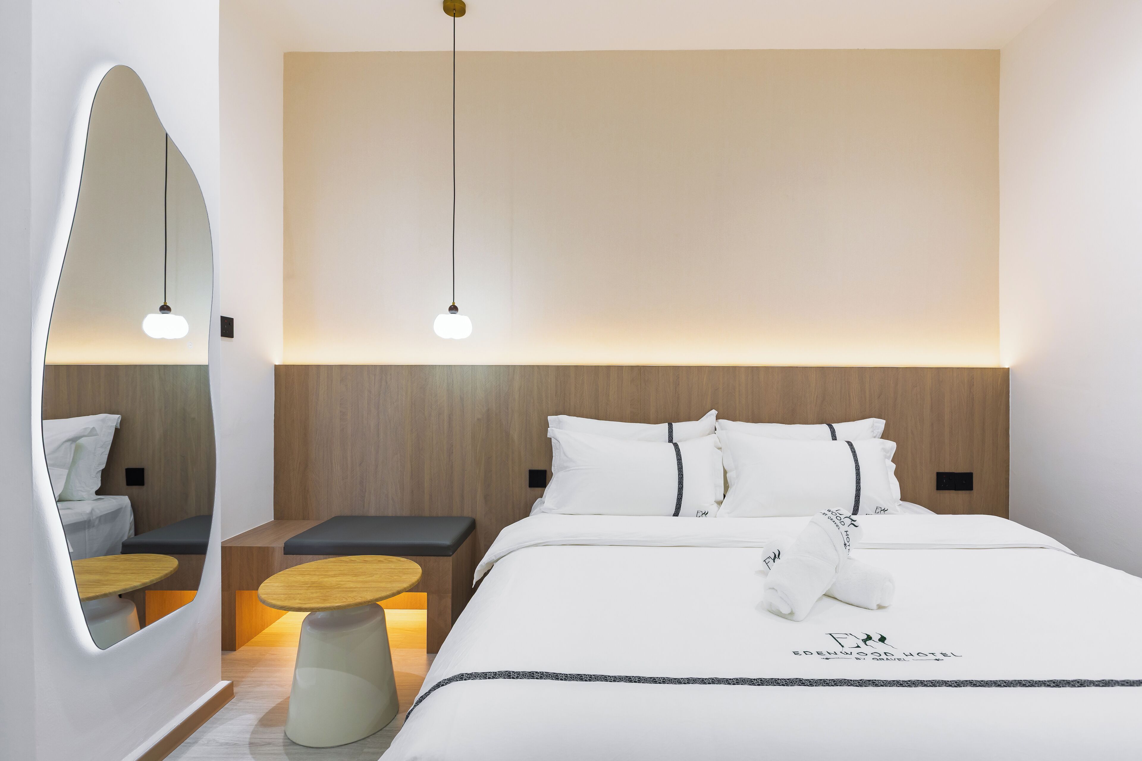 A modern hotel room with a large bed, bedside tables, a mirror, and pendant lighting.