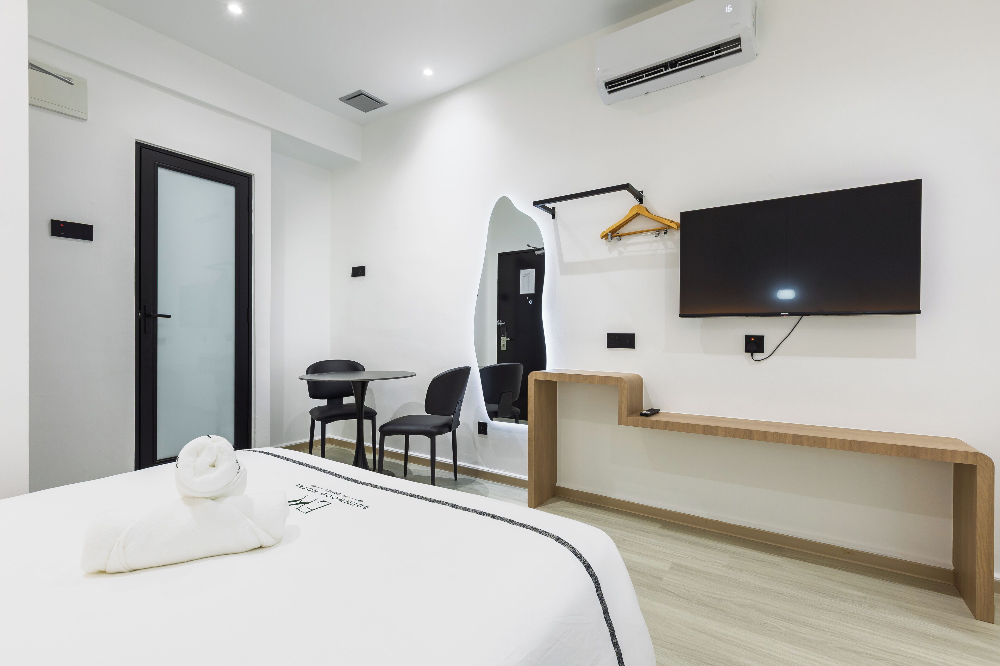 A modern hotel room with a bed, a desk, a chair, a TV, and a mirror.