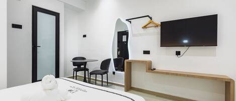 A modern hotel room with a bed, a desk, a chair, a TV, and a mirror.