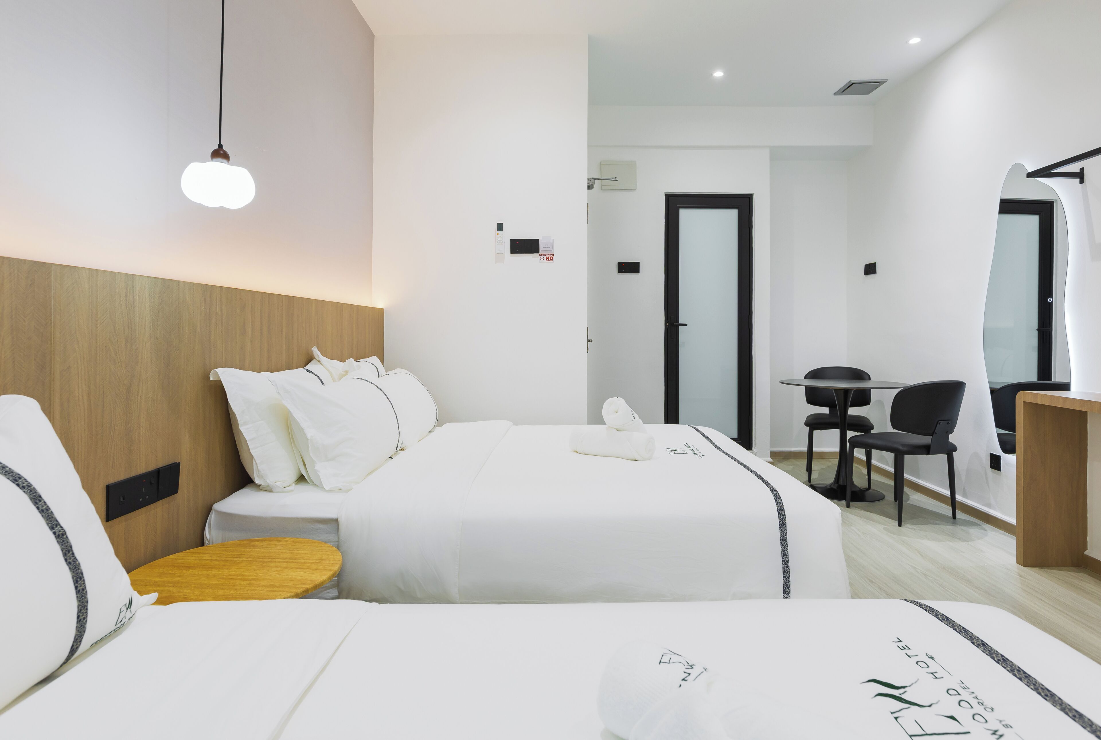 Habitación de hotel con dos camas, cabecero de madera, una mesita pequeña, un escritorio y una silla.