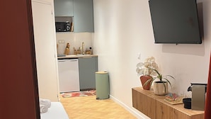 A hotel room with a bed, a small kitchenette, a TV mounted on the wall, and a wooden floor.