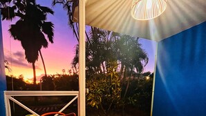 A patio with a round table, red chairs, a potted plant, and a view of palm trees against a sunset.