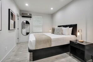 A modern bedroom with a bed, bedside tables, a mirror, and a window with blinds.