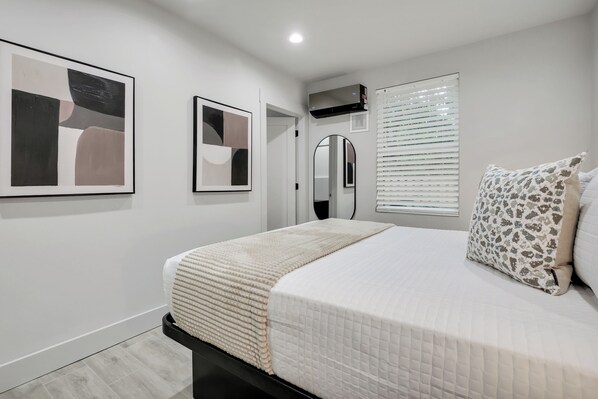 A bedroom with a bed, a mirror, and two framed artworks on the wall.