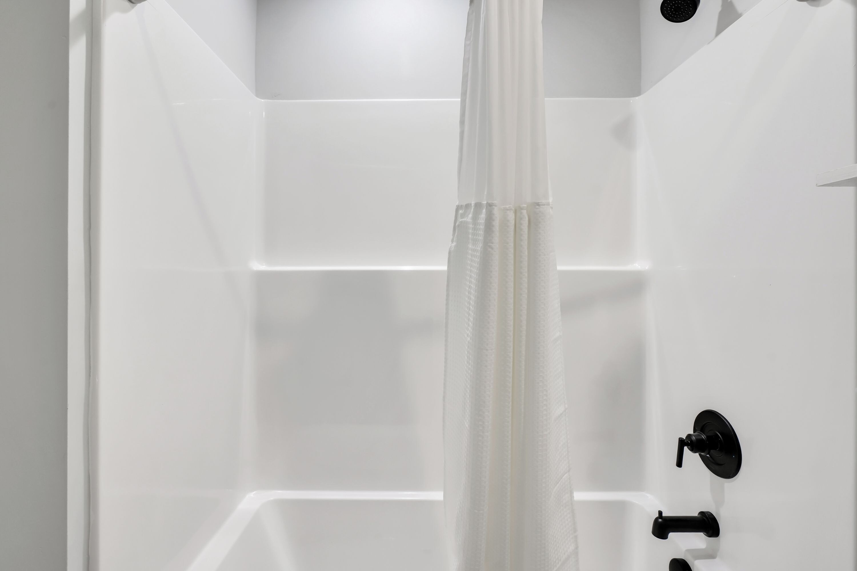 Eine weiße Badewanne mit Duschvorhang, einem schwarzen Wasserhahn und einem Drehknopf.