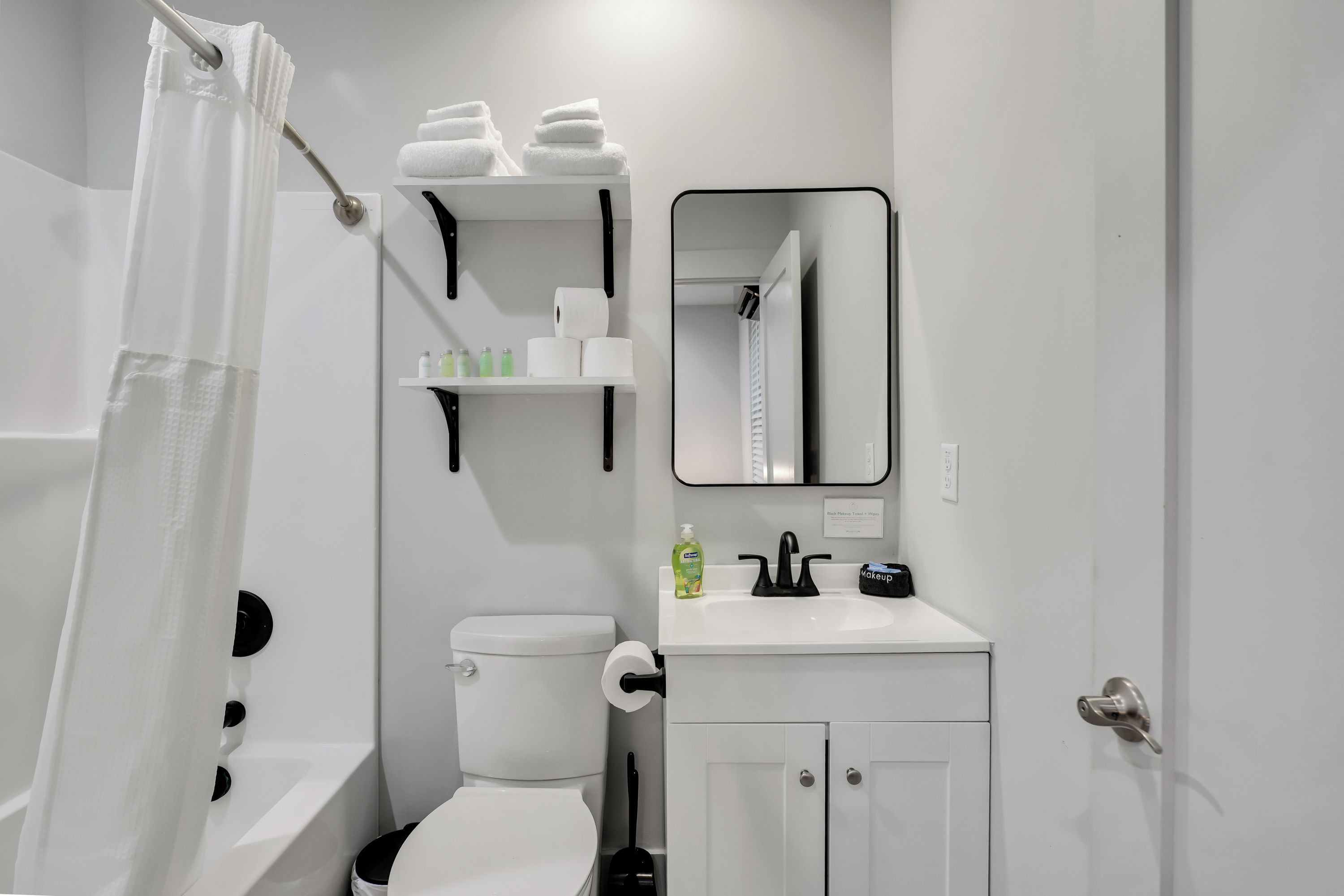 Ein modernes Badezimmer mit Toilette, Waschbecken und Spiegel. Über dem Waschbecken befinden sich Regale mit Pflegeprodukten und Handtüchern.