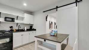 A modern kitchen with white cabinets, a black stove, and a wooden table with a chair. - The Jewel – Modern Retreat Near YMCA & Downtown (Wilmington)