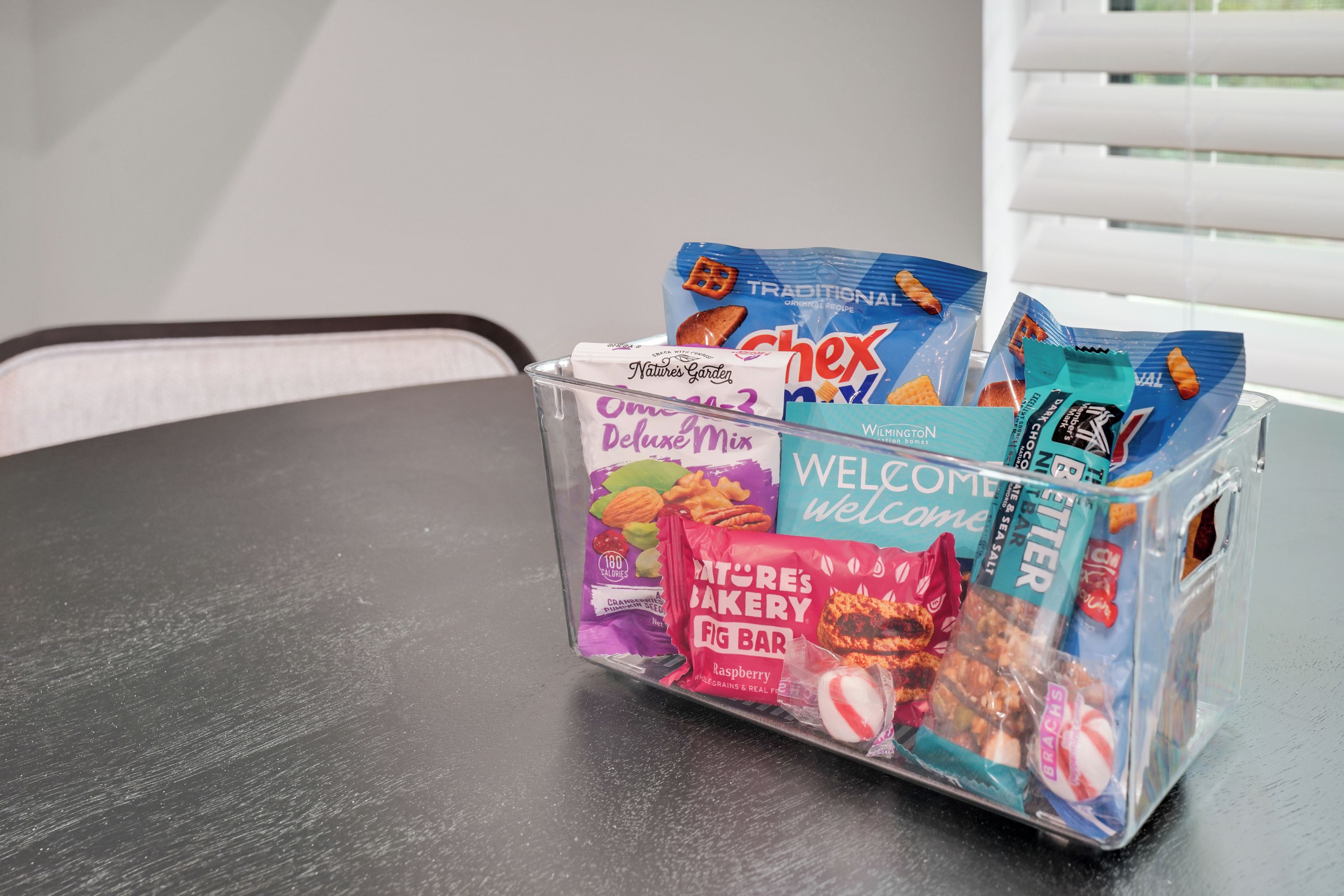 A clear plastic basket containing various snack items on a dark surface.