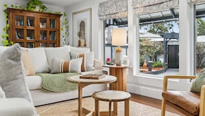 Een gezellige woonkamer met een bank, een salontafel en een fauteuil. Er is een houten kast en een raam met uitzicht op de tuin.