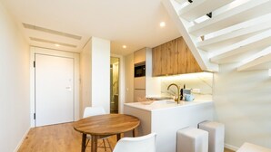 A modern kitchen with a wooden island, white chairs, and a staircase.