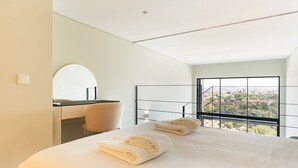 A modern hotel room with a large bed, a bathroom with a mirror, and a balcony with a city view.