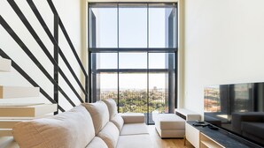 A modern living room with a large window, a sofa, a TV, and a staircase.