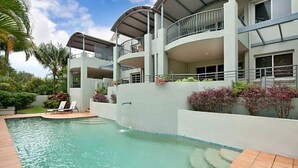 Ein modernes Hotel mit Pool, mehreren Balkonen und üppiger Bepflanzung.