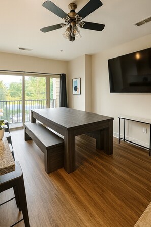 A modern living room with a dark wood table, a ceiling fan, and a flat-screen TV mounted on the wall. - Family & Group Retreat|3 Queens Beds + Pool Table 2nd (Birmingham)