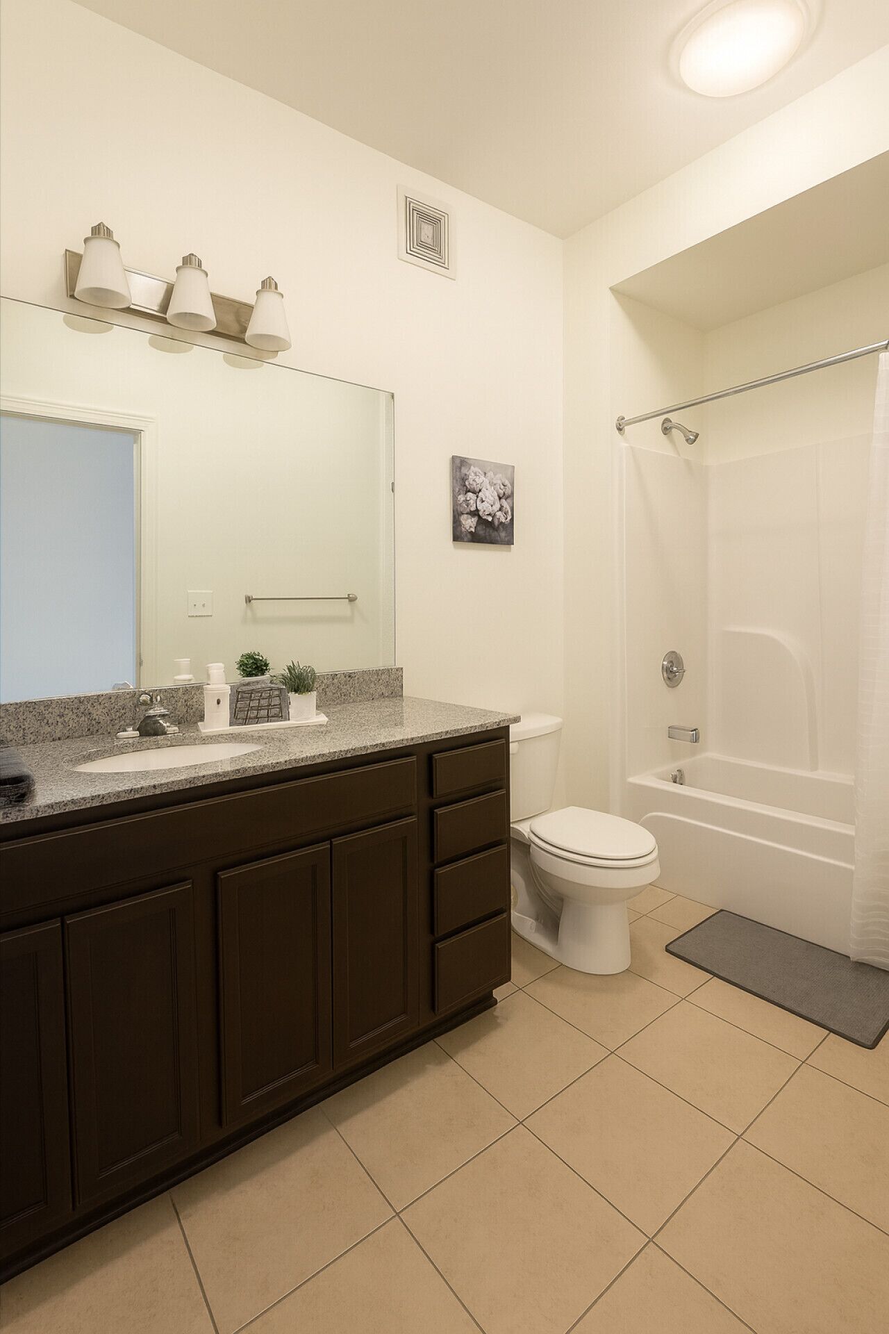 Un bagno moderno con lavabo su piano in granito, mobili contenitori in legno scuro, un water bianco, una vasca da bagno e una doccia.