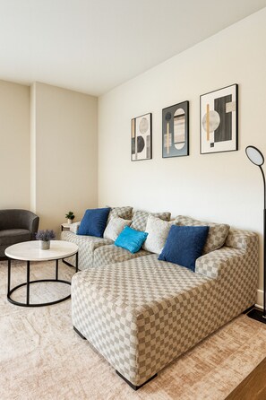 A living room with a checkered sofa, a round coffee table, a grey armchair, and a floor lamp. There are three framed artworks on the wall. - Family & Group Retreat|3 Queens Beds + Pool Table 2nd (Birmingham)