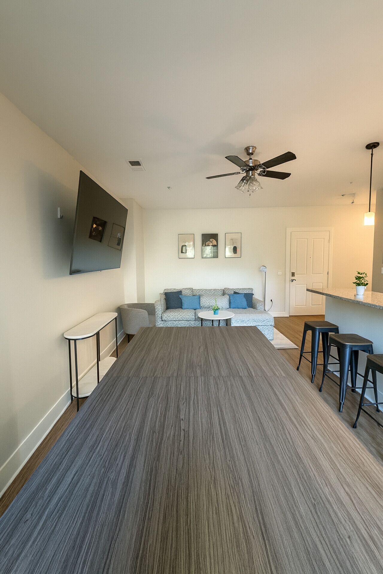 Uma sala de estar moderna com carpete cinza, um conjunto de sofá, uma área de jantar com bancos e um ventilador de teto.