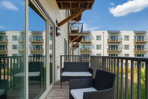Ein Balkon mit Korbmöbeln und einer Glastür, mit Blick auf eine Reihe moderner Wohngebäude.