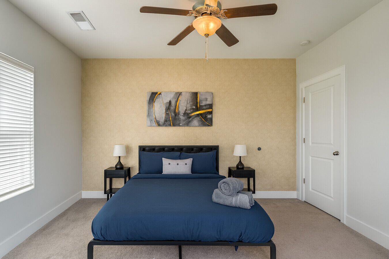 A bedroom with a bed, two bedside tables, a ceiling fan, a door, and a wall with a geometric pattern.
