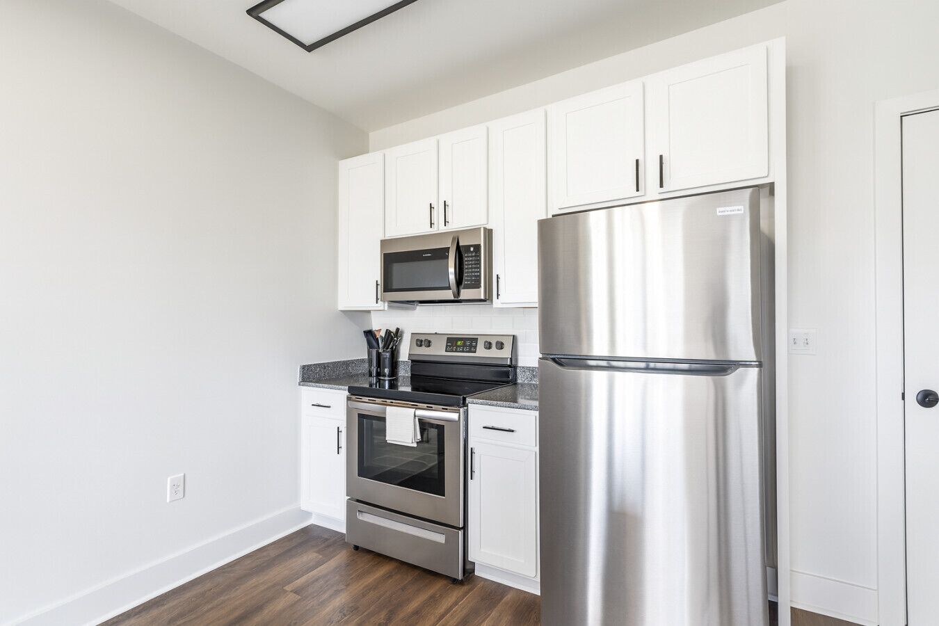 A modern kitchen with white cabinets, a stainless steel refrigerator, a microwave, and an oven.