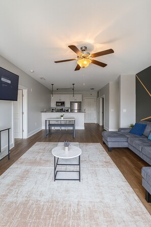 A modern living room with a grey sofa, a coffee table, and a ceiling fan. - 🏙 Luxury 2BR Condo | Steps from UAB Campus 5a (Birmingham)