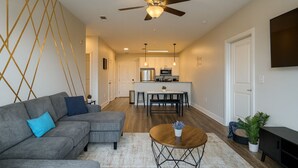 Un salon moderne avec un canapé d’angle gris, une table basse en bois et un ventilateur de plafond.