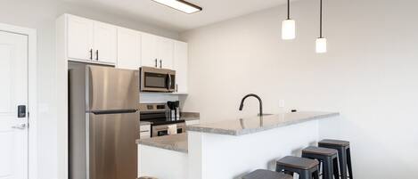 A modern kitchen with stainless steel appliances, a granite countertop, and bar stools.
