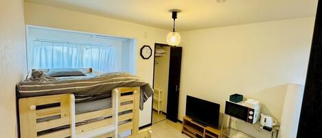 A compact room with a bunk bed, a small TV, a coffee machine, and a table with a remote control.
