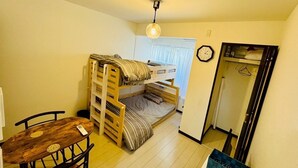A compact room with a bunk bed, a small table with chairs, a hanging light fixture, and a clock on the wall. - GUEST HOUSE TEN (Osaka)