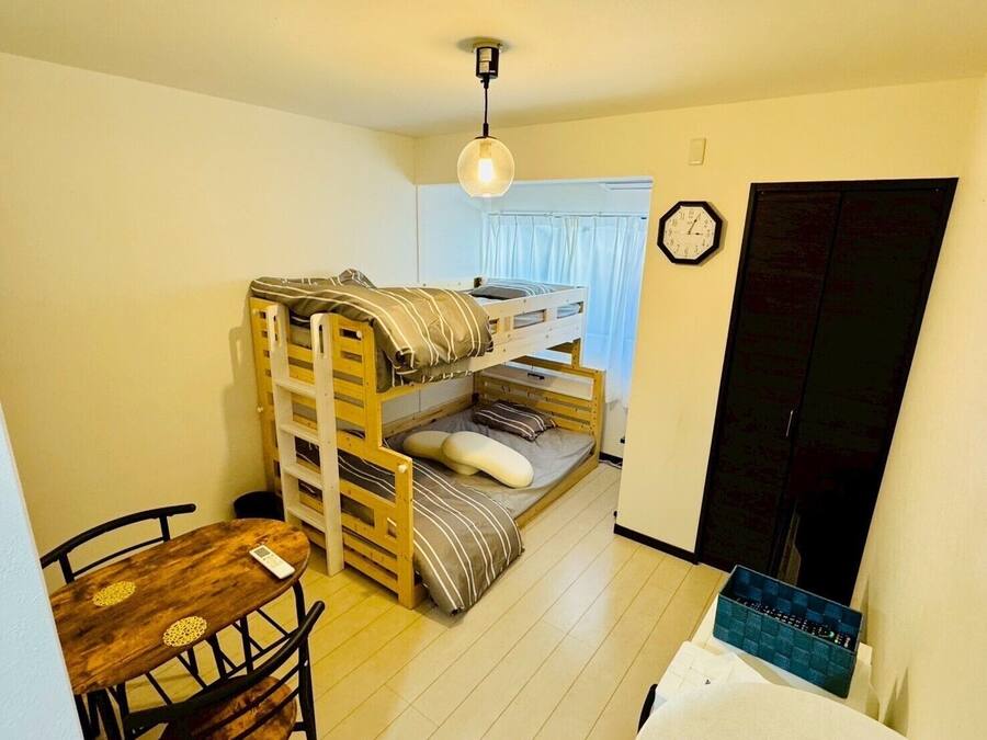 Ein kleiner, gemütlicher Raum mit einem Etagenbett, einem Holztisch mit Stühlen, einer Uhr an der Wand und einer Tür.
