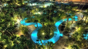 An aerial view of a resort with a winding pool surrounded by palm trees and tropical vegetation.