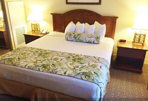 A hotel room with a large bed, a wooden headboard, two bedside tables with lamps, and a patterned carpet.