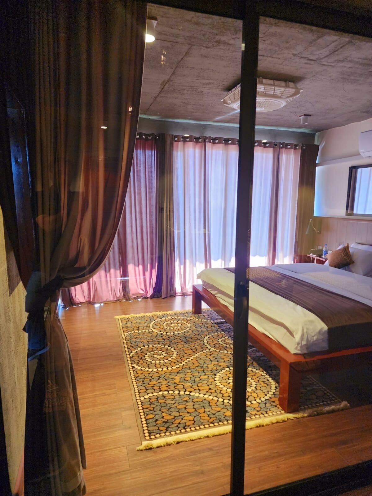 A bedroom with a bed, curtains, a patterned rug, and a ceiling fan.