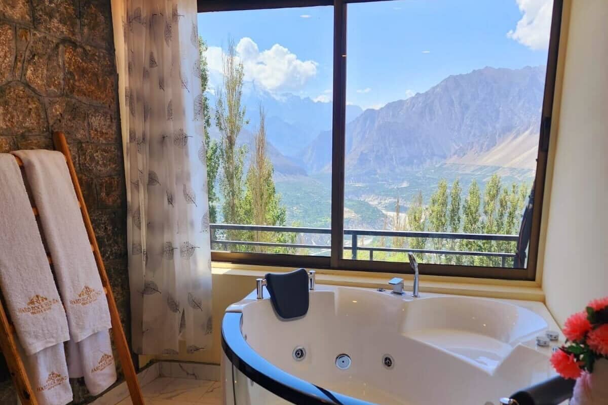 Un baño con una bañera grande, un perchero de madera, suelo de mármol y una ventana con vistas a la montaña.