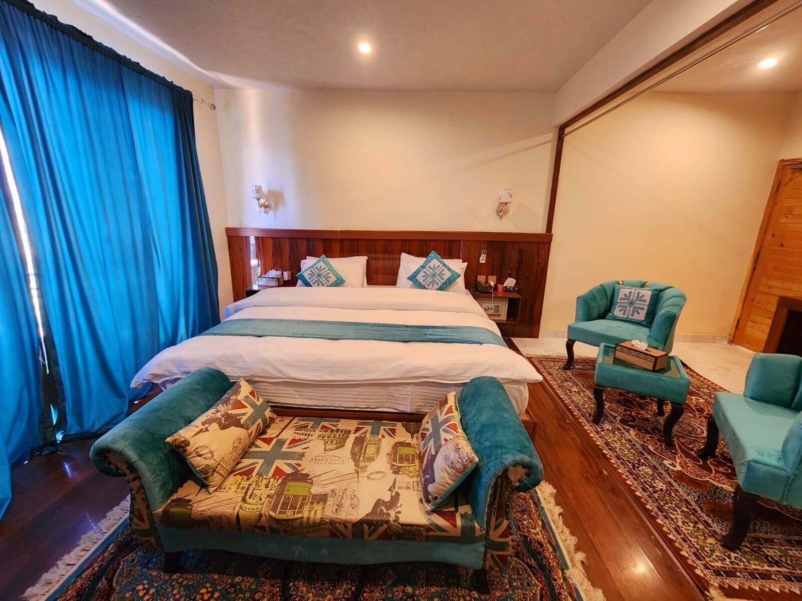 A hotel room with a large bed, two armchairs, a patterned sofa, and a wooden floor.