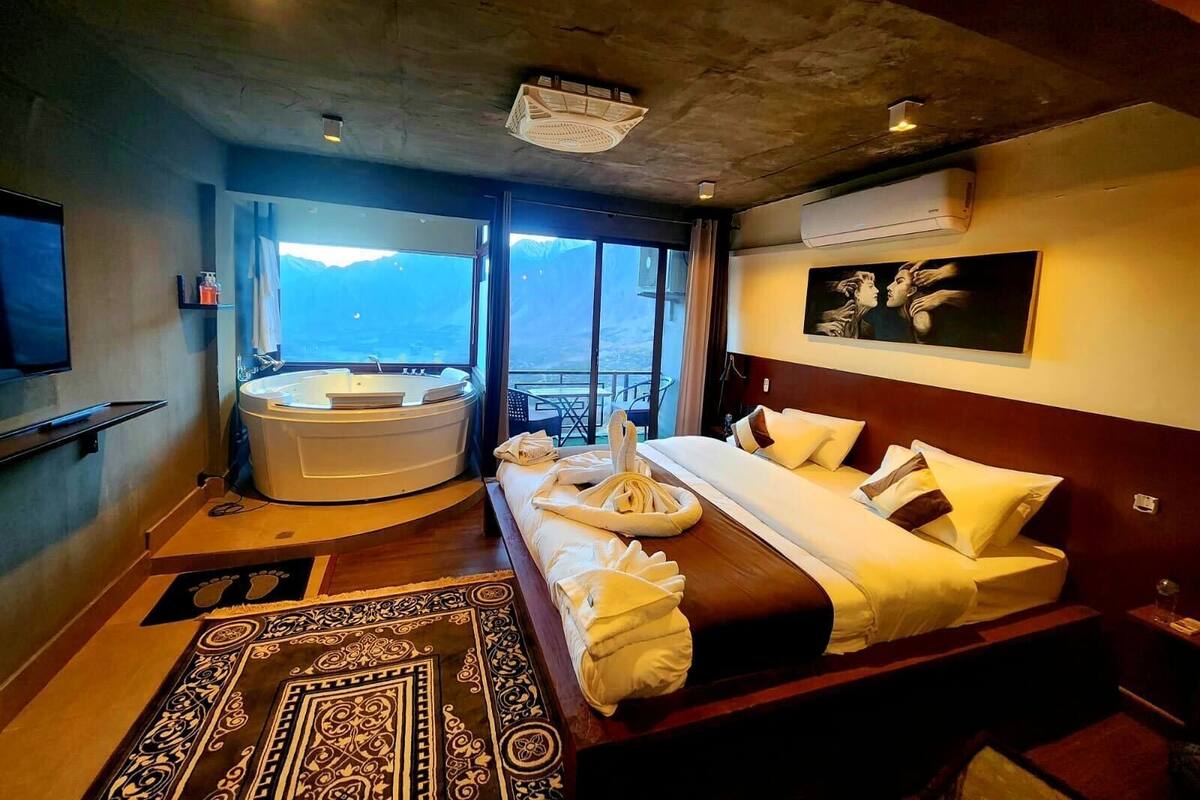 Una habitación de hotel moderna con una cama grande, un jacuzzi, un televisor y un balcón con vistas a la montaña.