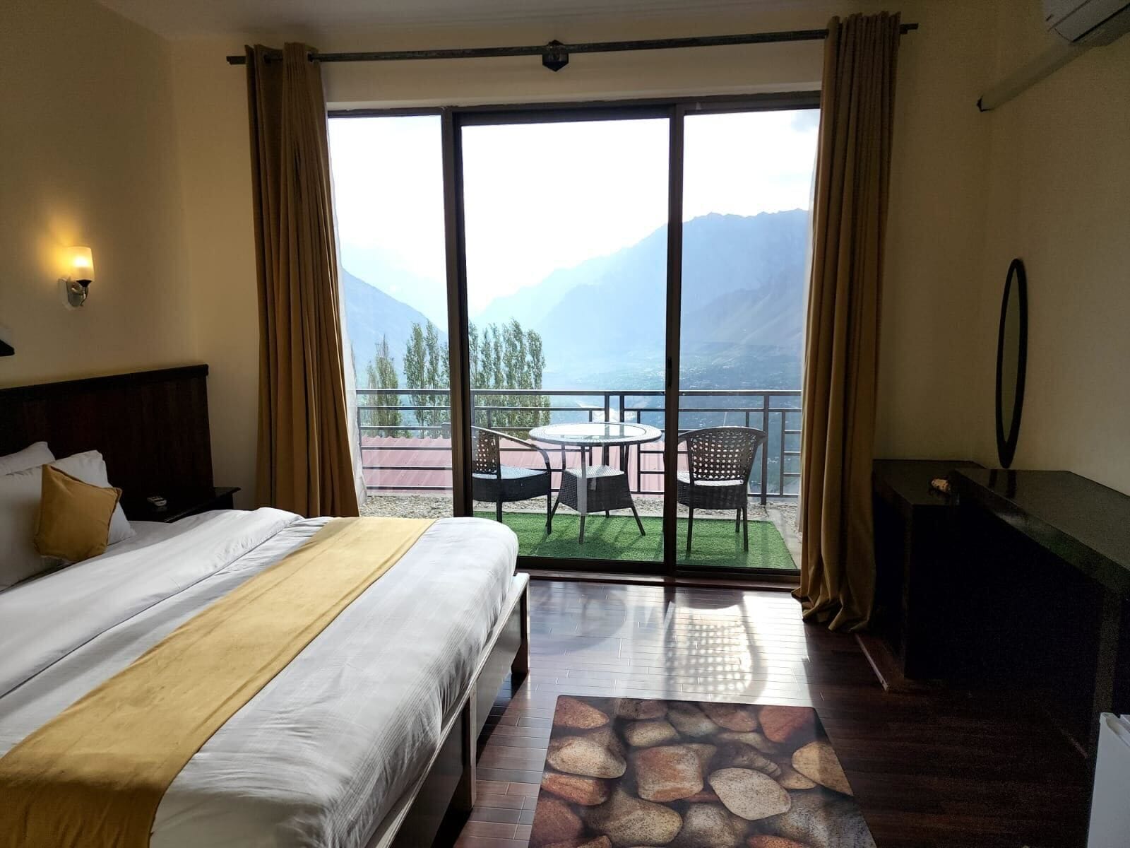 A hotel room with a bed, a desk, a chair, and a balcony with a table and chairs.