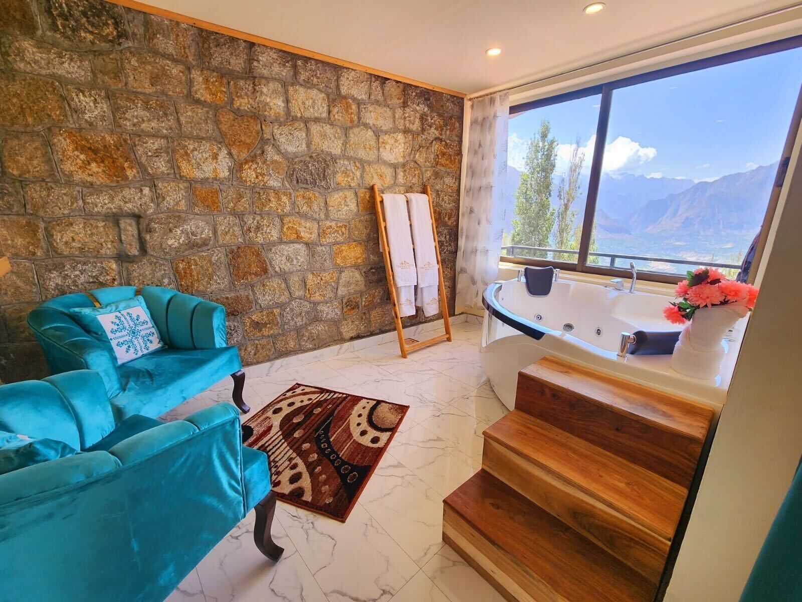 A room with a stone wall, a blue sofa, a wooden staircase, and a view of mountains through a large window.