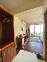 Quarto com armário de madeira, pequena cozinha compacta, varanda com mesa e cadeiras, e uma cama.