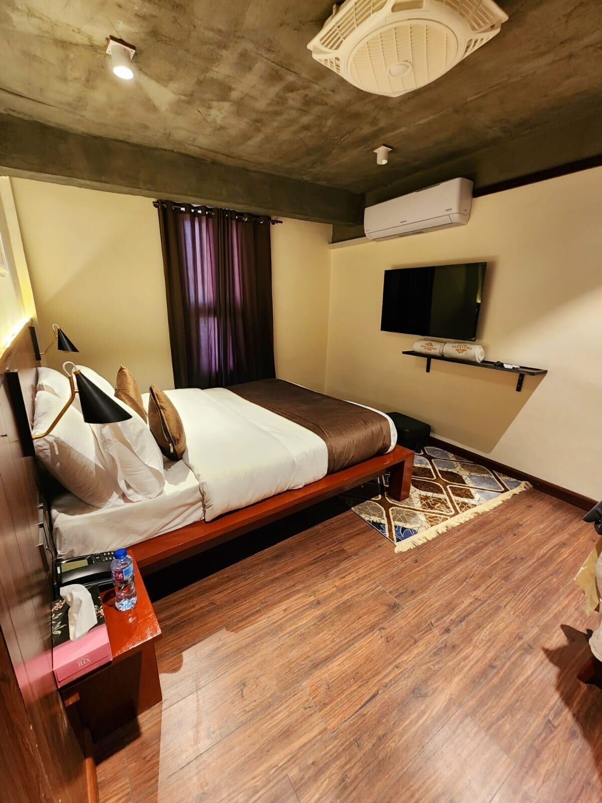 A bedroom with a bed, a TV, an air conditioner, and a wooden floor.