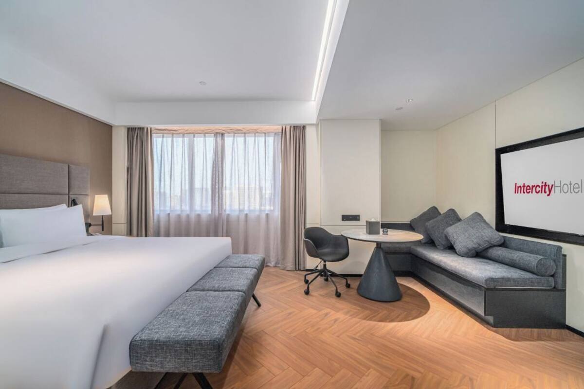 Ein modernes Hotelzimmer mit einem großen Bett, einem grauen Sofa, einem kleinen Tisch und einem Sessel.