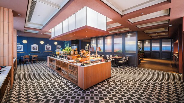 Un moderno vestíbulo de hotel con un mostrador de recepción de madera central, zonas de estar y grandes ventanales que ofrecen vistas.